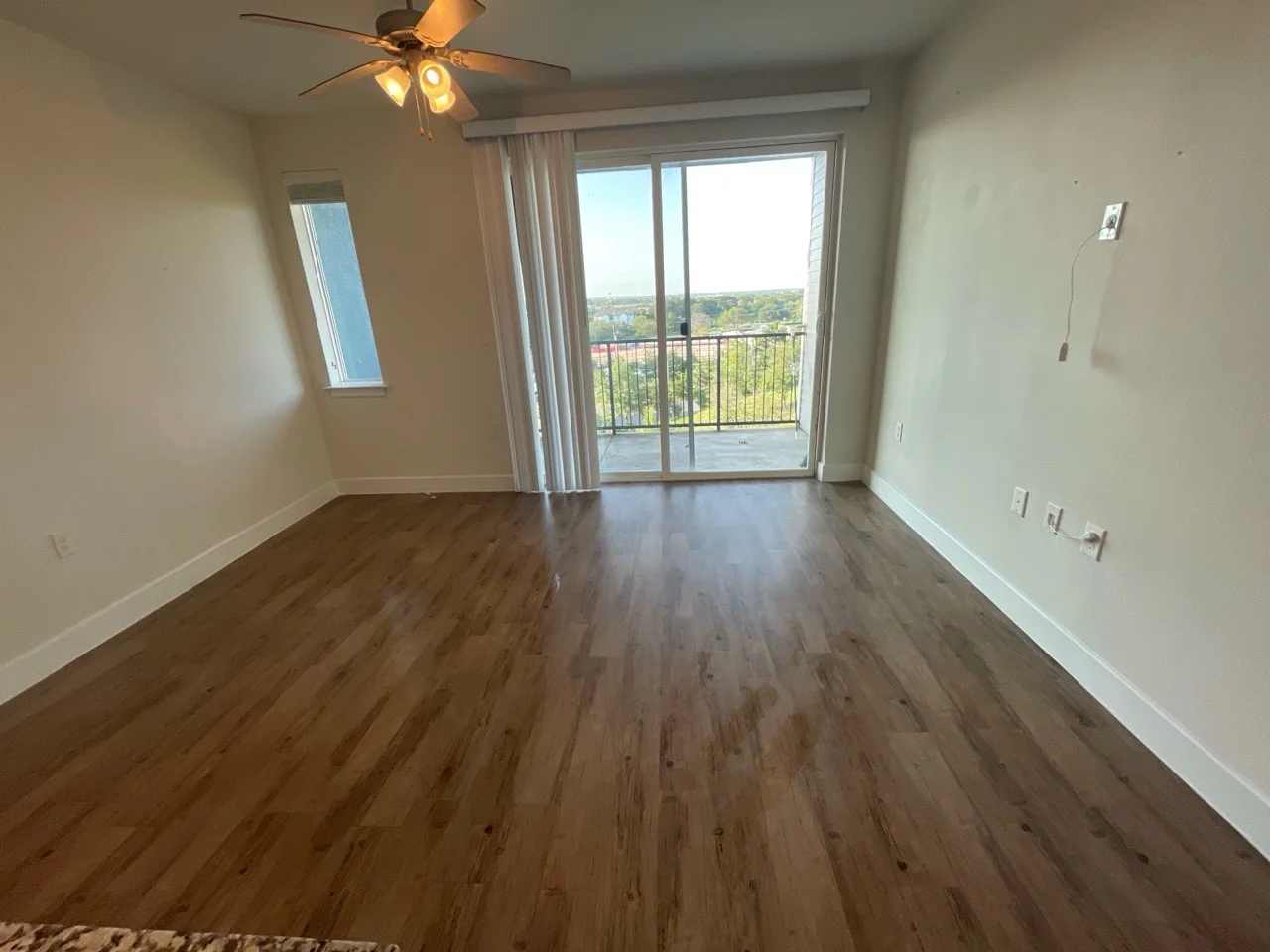 After cleaning: the same empty living area, photographed from a wider, different camera angle, with clean exposed floors and balcony door.